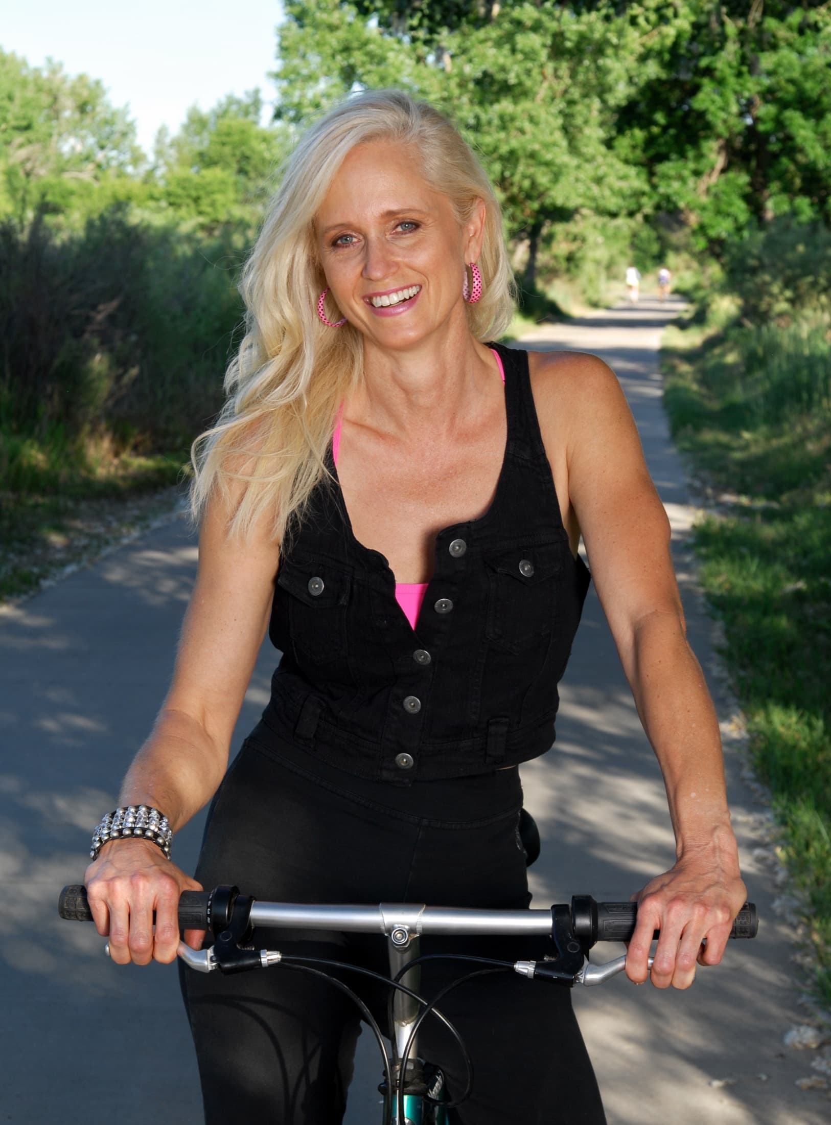 A woman riding a bicycle along a tree-lined path, smiling
