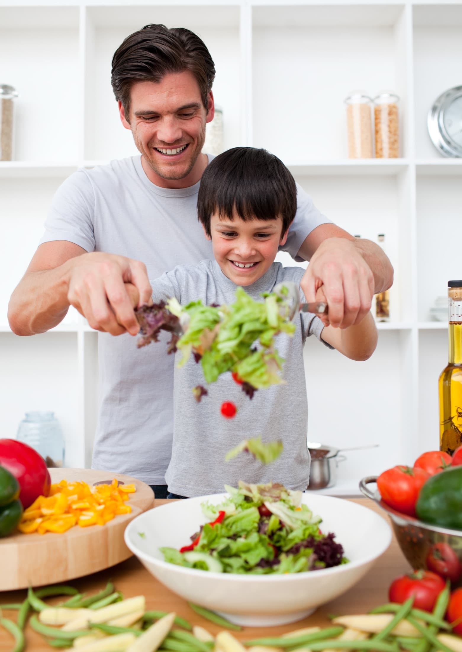 A father and his young son tossing a salad together in a kitchen